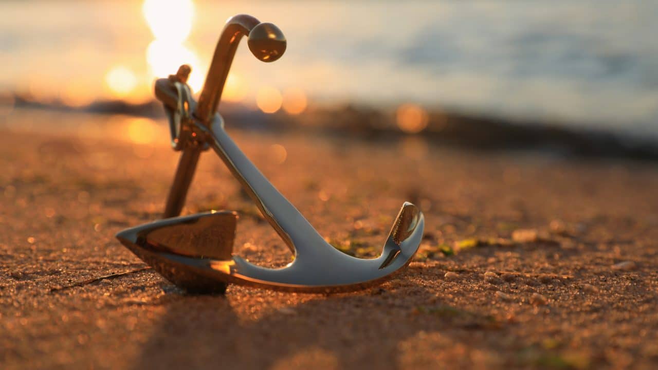 Metal anchor on shore near river at sunset