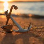 Metal anchor on shore near river at sunset