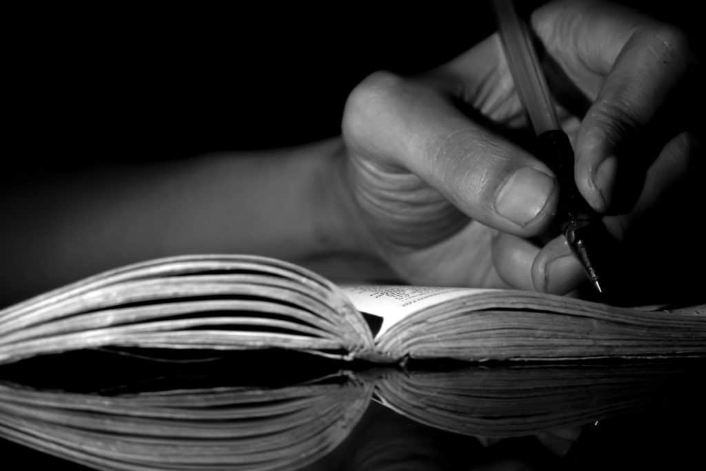 Close up of a man s hand writing on paper at night hand writing a letter writing in a diary